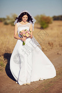 带着天然花圈的美丽笑容新娘站在金色的夏日田里手握着图片