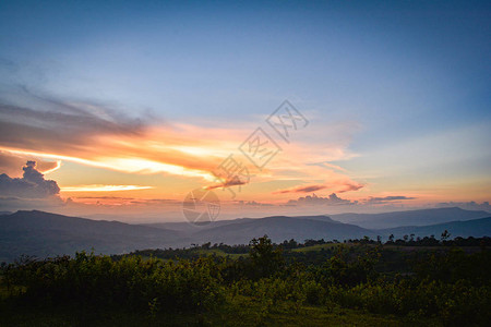 山丘上黄色和蓝色的天空与山地风景的田野日落美景背图片