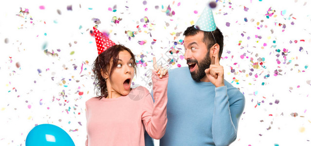 配着气球和生日帽子的情侣想要在派对上用彩蛋来举起手指时图片