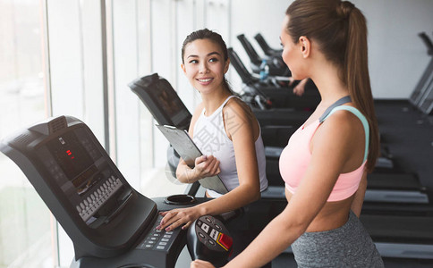 教练在健身房锻炼期间与跑步机上的女孩图片