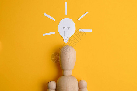 发现商业想法或启动的概念在涂漆灯泡下的黄色背景的Woodenman图片