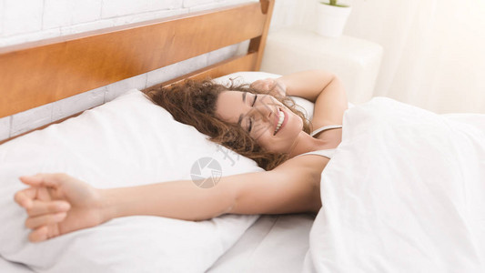 在床上醒来的年轻女子微笑和伸展全图片