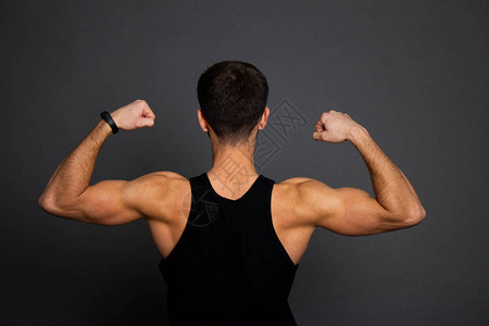 英俊的年轻人站在黑色的背景和弯曲的肌肉肌肉运动健美身模型锻炼后摆姿图片