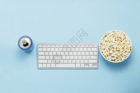 键盘和锡罐与饮料能量饮料蓝色背景上的一碗爆米花图片