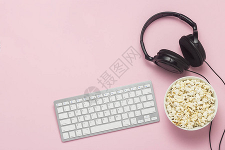 键盘耳机和粉红色背景的一碗爆米花观看电影表演体育在PS上网上游戏的概念平躺背景图片