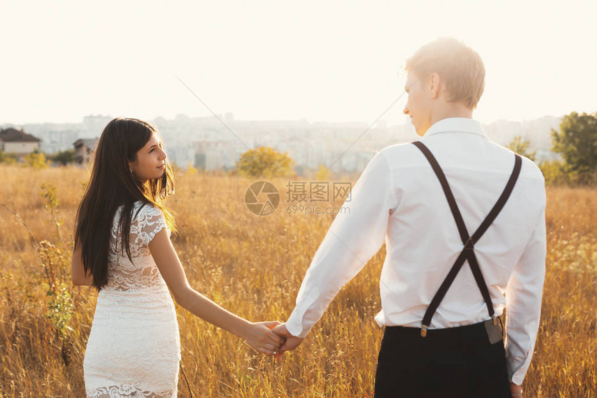 一名年轻女子与男友手牵在草地上行走的后视镜头一对夫妇在阳光明媚的日子里享受着在地平线上的城市漫图片