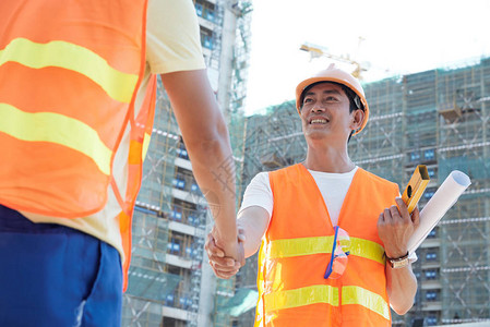在建筑工地微笑的亚洲工程师在承包人握图片