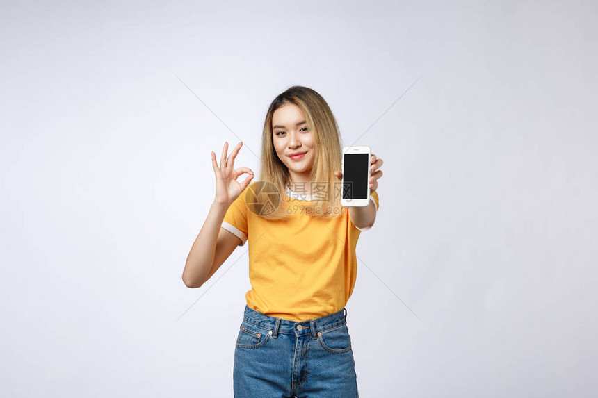 穿着黄色衬衫的亚洲年轻女在白色背景上展示了好牌子手持机图片
