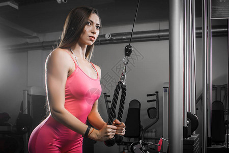 穿着运动服的黑发女运动员在健身房的模拟器上摇晃手三头肌二头肌图片