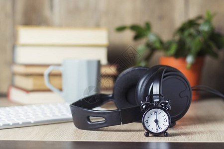 办公桌上的闹钟耳机和键盘与书籍办公室概念工作日小时工资工作时间表在图片