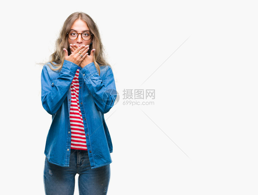 美丽的金发年轻女人戴着眼镜身穿孤立背景的眼镜以错误之手遮住嘴部震图片