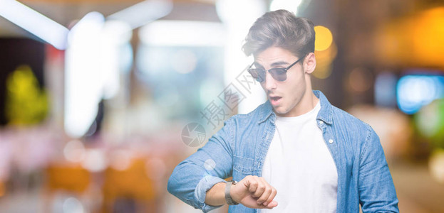 英俊的年轻帅哥穿着太阳镜背着孤立的背景看着钟表时间图片