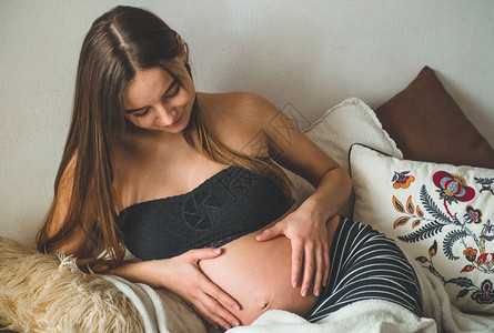 有吸引力的孕妇坐在床上抱着她的肚子怀图片