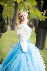 穿着蓝仙女服装和秋天公园白色短皮大衣的图片