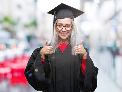 身着研究生制服的金发年轻女子在孤立的背景成功征兆下图片