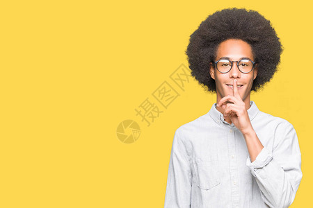 戴着眼镜的非洲年轻男子要求用手指在嘴唇上保持安静沉默和秘密概念图片