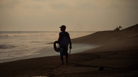 渔夫在沙滩日落时从海边拉网渔图片