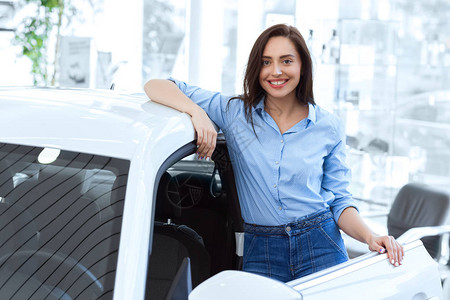 拍到一个有魅力的年轻女人在汽车经销商复制站旁边站在她新买的图片