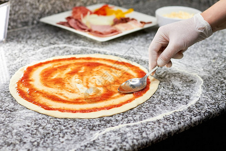 用勺子在比萨饼皮上涂抹酱汁关闭手厨师巧妙地用特制的传统酱汁图片