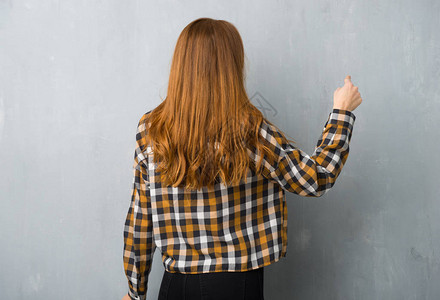 年轻的红发女孩在grunge墙上用食指点图片