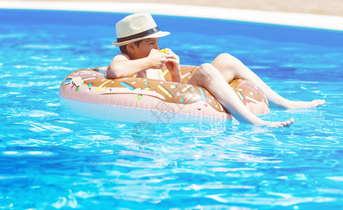 可爱的小男孩在带橘子的游泳池里玩有趣的充气甜圈浮环图片