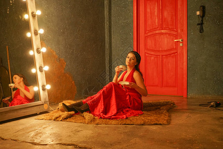穿着红裙子的漂亮女孩坐在毛地毯上喝着白图片