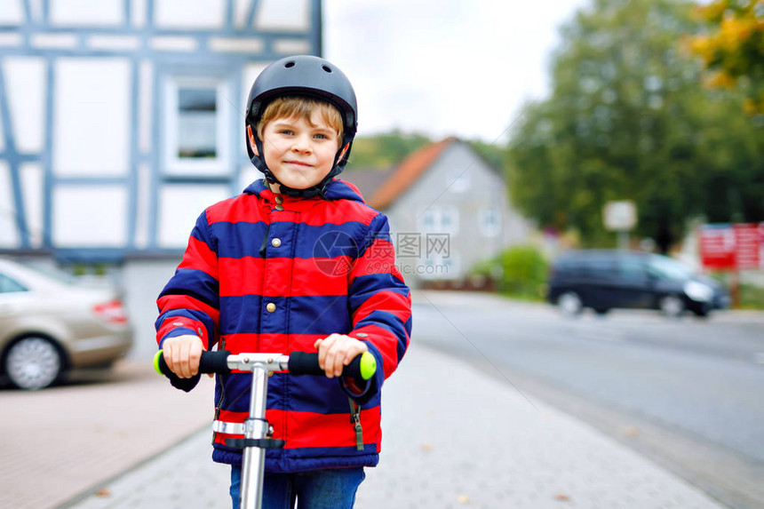 可爱的小学生男孩戴着头盔骑在公园质的滑板车上冬季春季或秋季的儿童户外活动穿着五颜六色时尚衣服的有图片