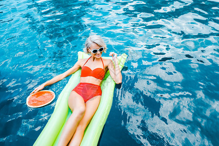 穿着泳衣的快乐搭针女孩在游泳池和西瓜的绿色充图片