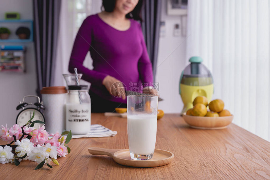 厨房桌和牛奶杯在妇女切水果背景上从图片