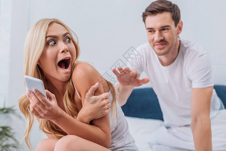 丈夫在床上使用智能手机接触惊吓的年轻妻子图片