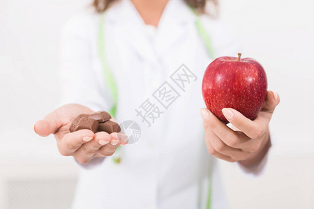 食物饮食选择困境女营养师提供新鲜苹果替代不健康的牛奶巧克图片