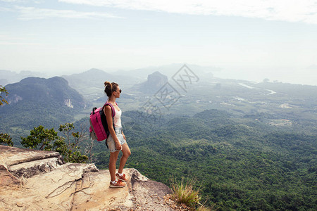 年轻女旅行者背着包站在山顶并享图片