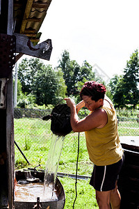 一个女人用井里的天然水填充金属盆的侧视图勤劳的园丁收集水为旱季做准备日常家图片