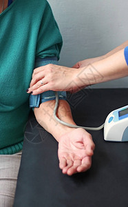 年长妇女用数字血压监测器量压力坐图片