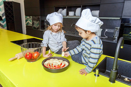带厨师帽的小女孩和男孩在厨房准备烤自制苹果派图片