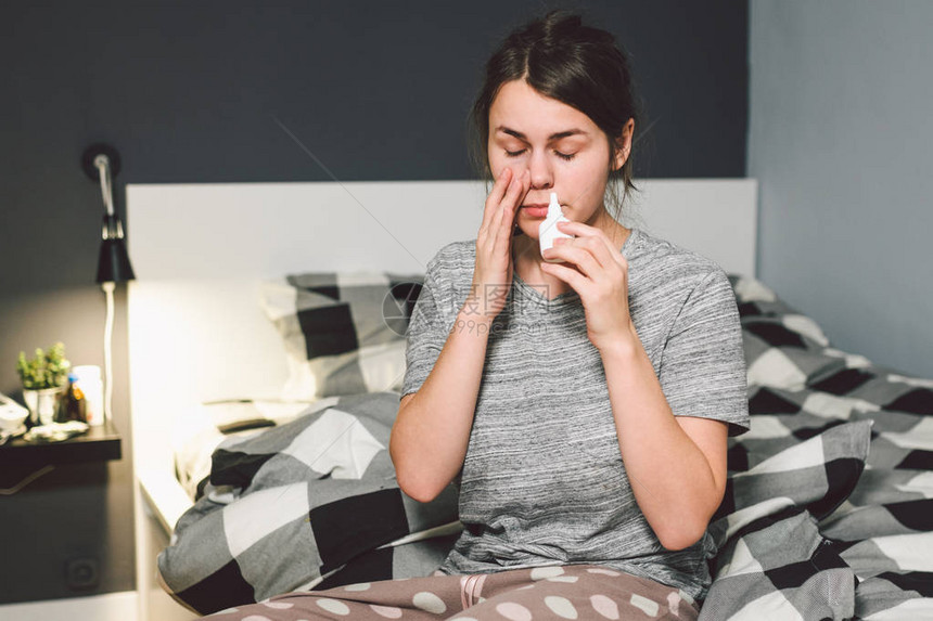 主题是季节感冒流鼻涕流感感染在家卧室床上的年轻白种女人在她的鼻子里喷药滴鼻涕过敏图片