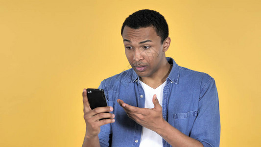 使用黄色背景孤立的智能手机在震撼中的非洲青年男图片