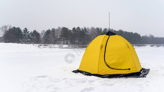 以莲花的形式黄色钓鱼冬天帐篷站立在河的白雪皑的冰上图片