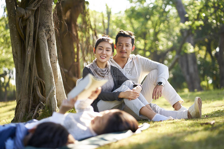 两个亚裔小男孩和女孩躺在草地上玩得开心读一本书图片