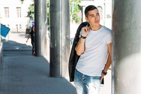 穿着白色T恤黑色皮夹克和蓝色破牛仔裤的年轻帅哥在街上图片