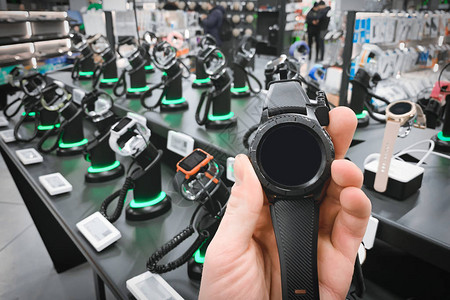 手持智能手表的人特写在货架上的手表背景上在科技商店图片