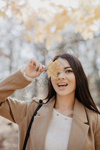 年轻女子拿着黄色叶子遮着秋天公图片