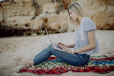 身着便衣手持笔记本电脑坐在海边的图片