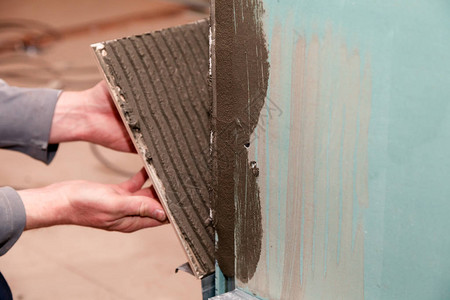 特写专业建筑工人的手在浴室里用粘合剂粘住瓷砖图片