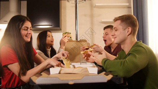 一群年轻朋友坐在厨房吃披萨吃着图片