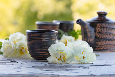 陶瓷杯茶壶和白狗玫瑰在花园的旧木制桌子上图片