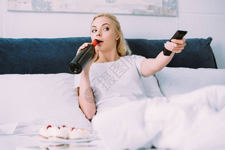 妇女独自在床上庆祝生日时喝酒和看电视图片