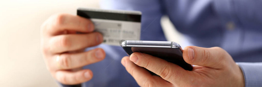 西装革履的男手臂拿着信用卡和电话使转移特写输入客户折扣计划编号或填写个人凭证密码登录账户时的反图片