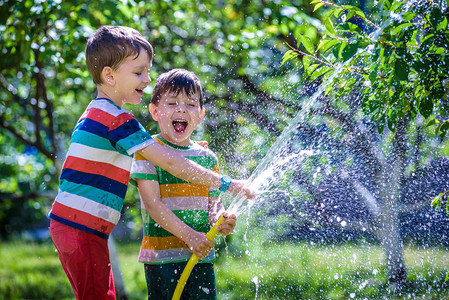 可爱的小男孩在花园里用浇水软管浇水背景图片
