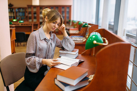 年轻漂亮的女人在大学图书馆的桌子上看书图片